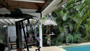 An outdoor gym area with exercise equipment, a pool, and lush tropical plants. - Melbourne Beach getaway, Surfing, Birdwatching, nature. fishing. (Melbourne Beach)