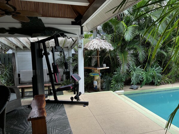 An outdoor gym area with exercise equipment, a pool, and lush tropical plants.
