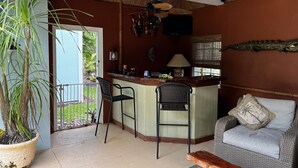 A kitchen area with a bar, two chairs, a sofa, and a large potted plant. - Melbourne Beach getaway, Surfing, Birdwatching, nature. fishing. (Melbourne Beach)