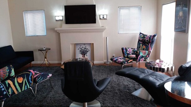 Un salon moderne avec une cheminée, des canapés en cuir noir, un fauteuil coloré et un téléviseur à écran plat fixé au-dessus de la cheminée.