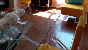 Un salon moderne avec une table basse en verre, un canapé agrémenté d’un coussin bleu, un meuble avec des portes en verre et une affiche représentant un bâtiment.