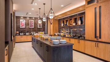 Una cocina moderna con armarios de madera, una isla central con platos y lámparas colgantes.