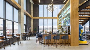 Eine moderne Bar mit hohen Decken, großen Fenstern und einer zentralen Bar mit Sitzhocker.