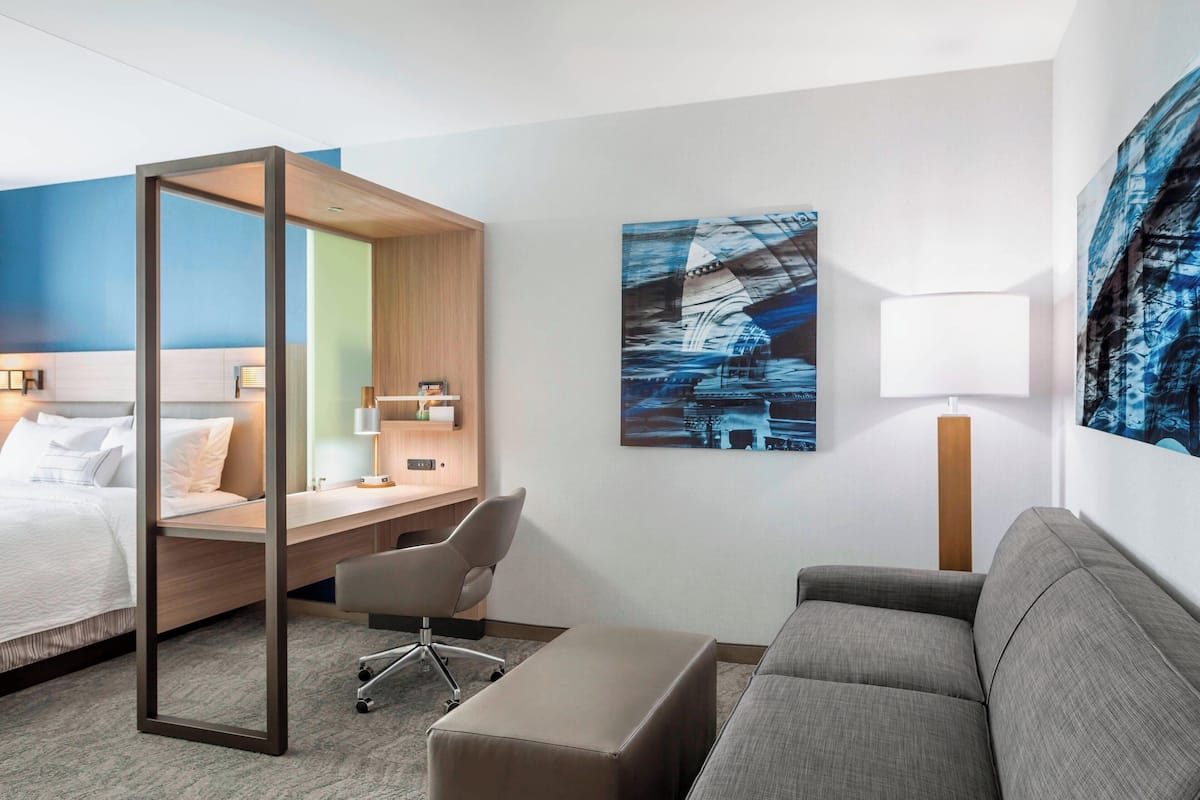 A hotel room with a bed, desk, chair, sofa, and artwork on the walls.
