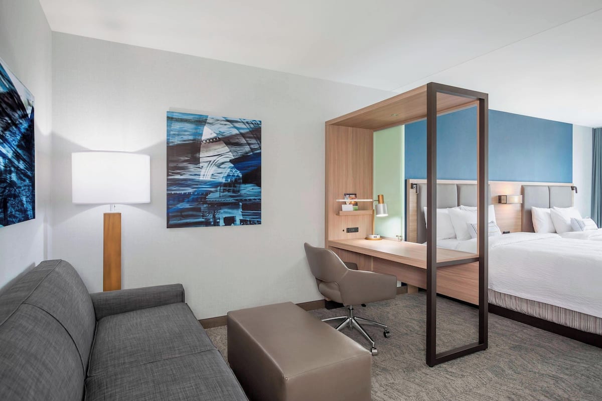 A hotel room with a bed, a desk, a chair, a sofa, and a lamp.