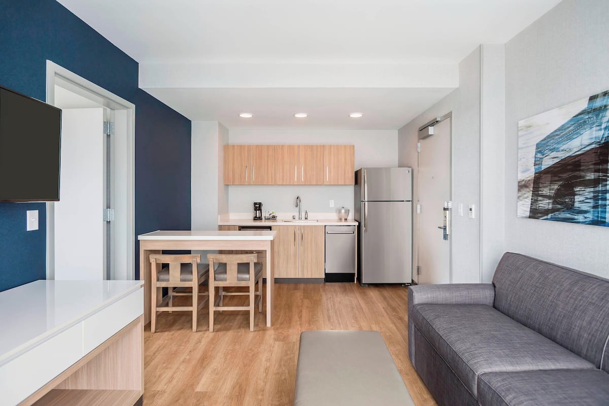 A modern kitchen with wooden cabinets, a stainless steel refrigerator, and a dining area with a table and chairs.