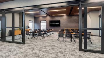 A conference room with a brick wall, a large screen, and multiple tables with chairs.