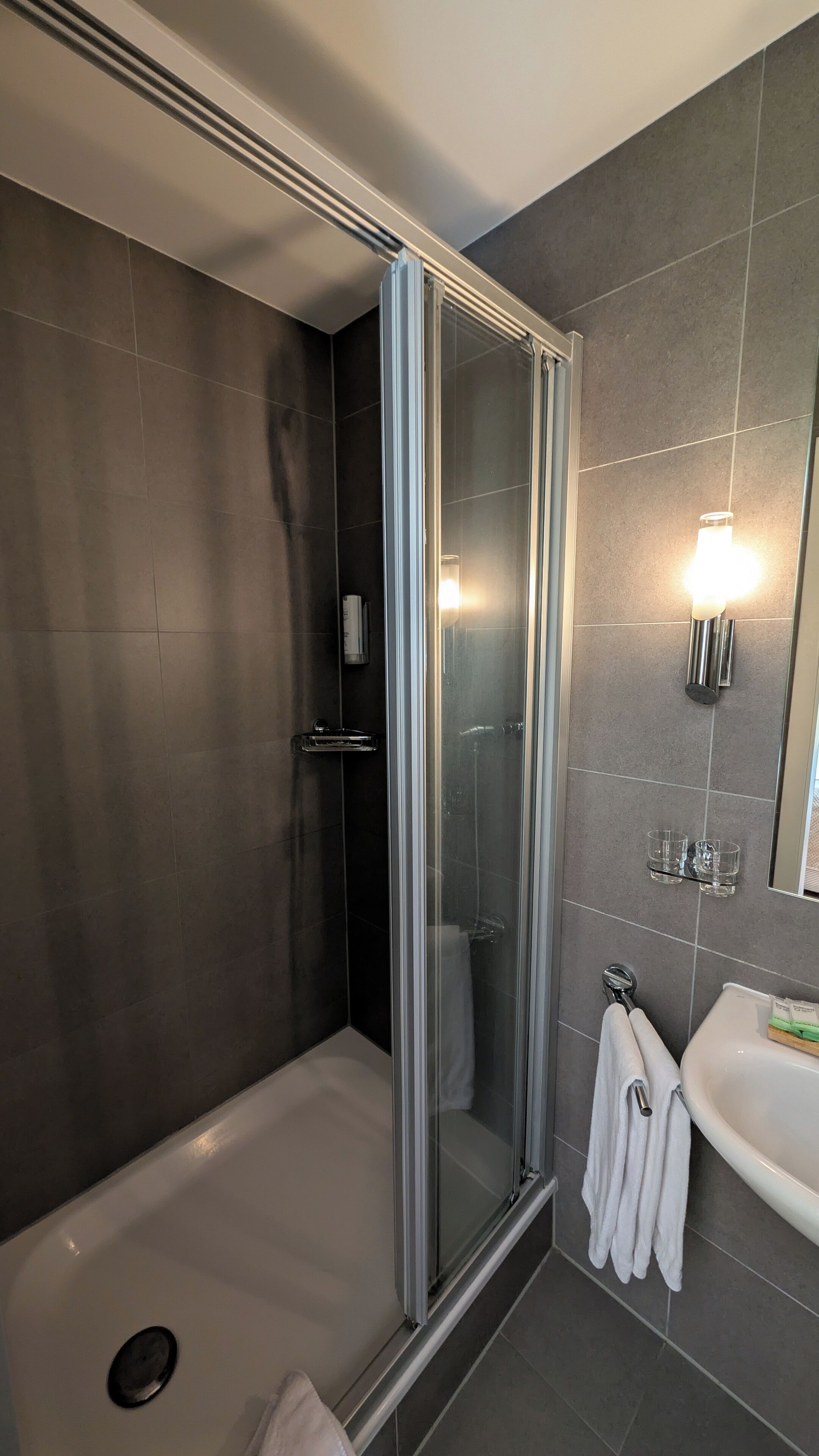 A modern bathroom with a glass-enclosed shower, a white sink, and a mirror with wall-mounted lights.