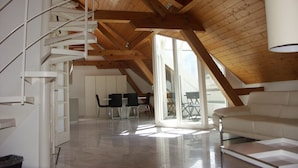 A spacious loft with a high ceiling, wooden beams, a spiral staircase, a dining area with chairs, and a sofa. - Hotel Harder Minerva (Interlaken)