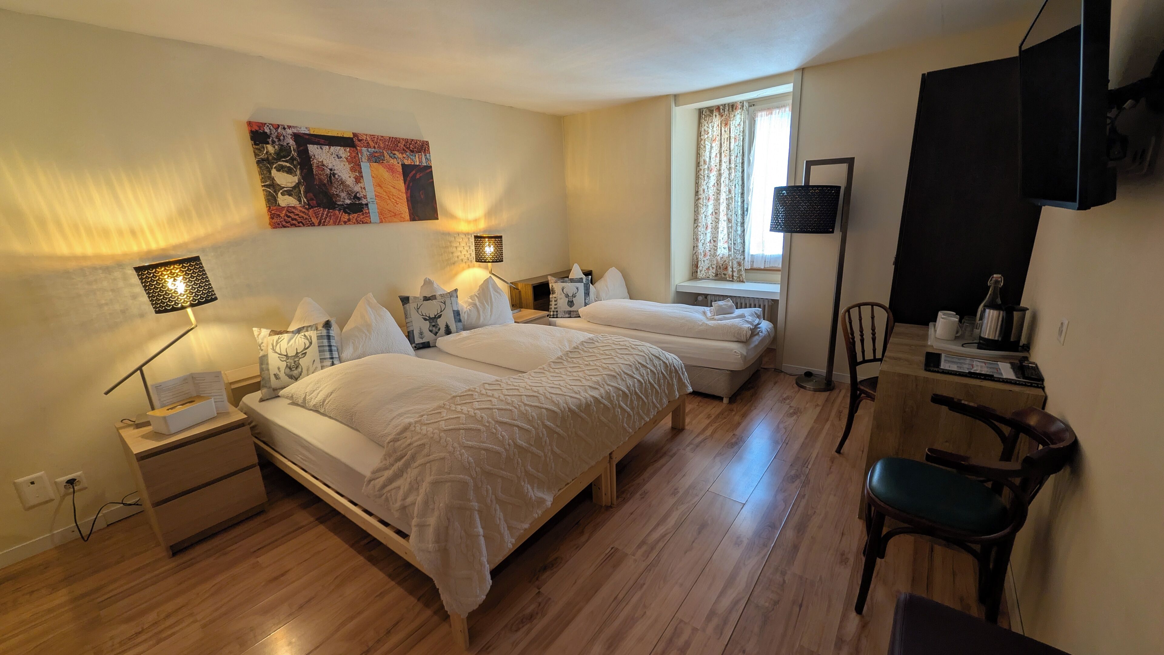 Une chambre avec deux lits, un bureau, une chaise, une télévision et une fenêtre avec des rideaux.