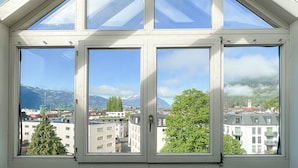 A room with a large skylight window offering a view of a cityscape, mountains, and trees. - Hotel Harder Minerva (Interlaken)