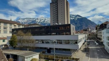 A modern building with a flat roof and large windows, surrounded by a small green area and a street with cars.