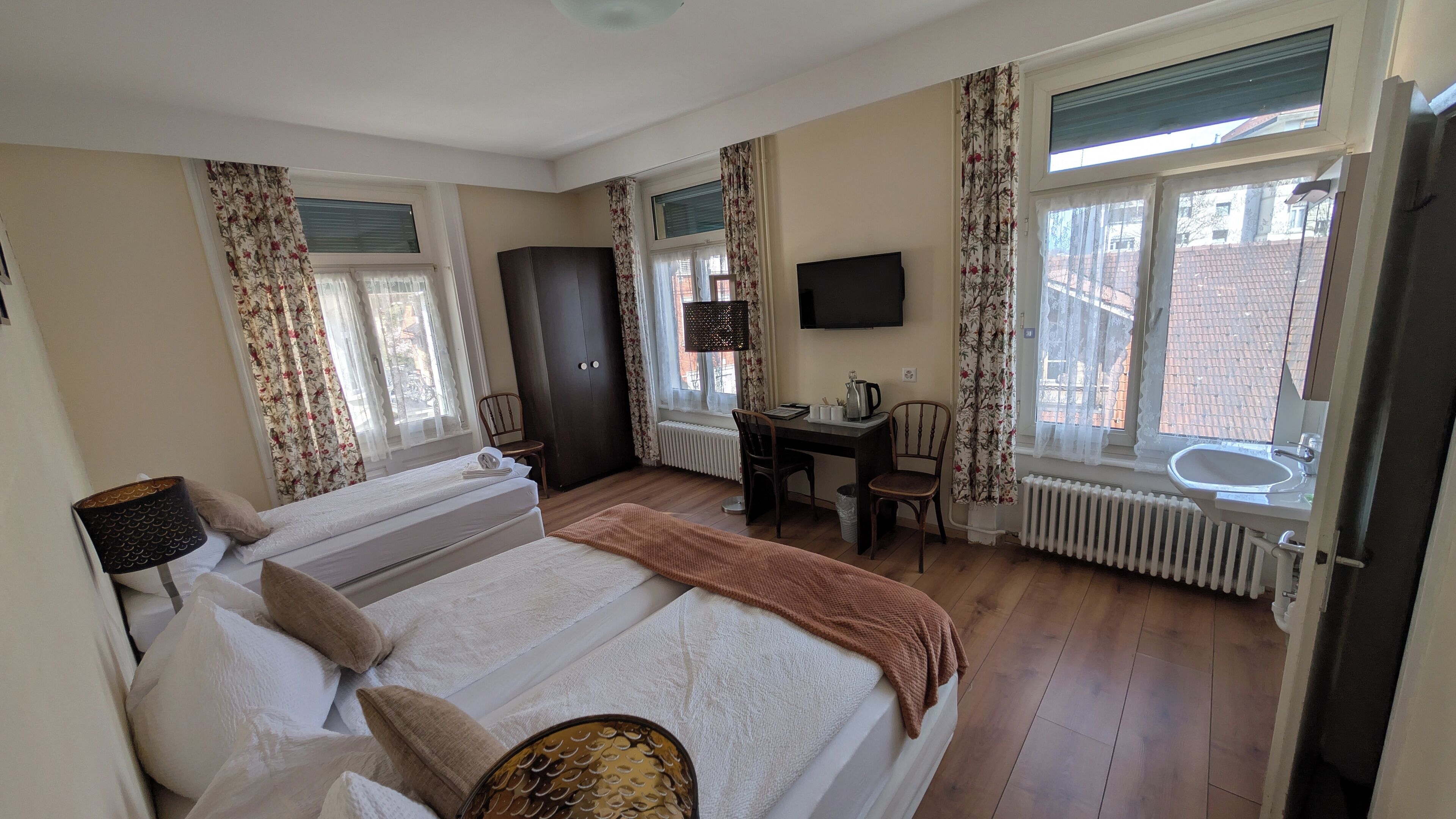 Ein Hotelzimmer mit Bett, Schreibtisch, Stuhl, Fernseher und einem Fenster mit Vorhängen.