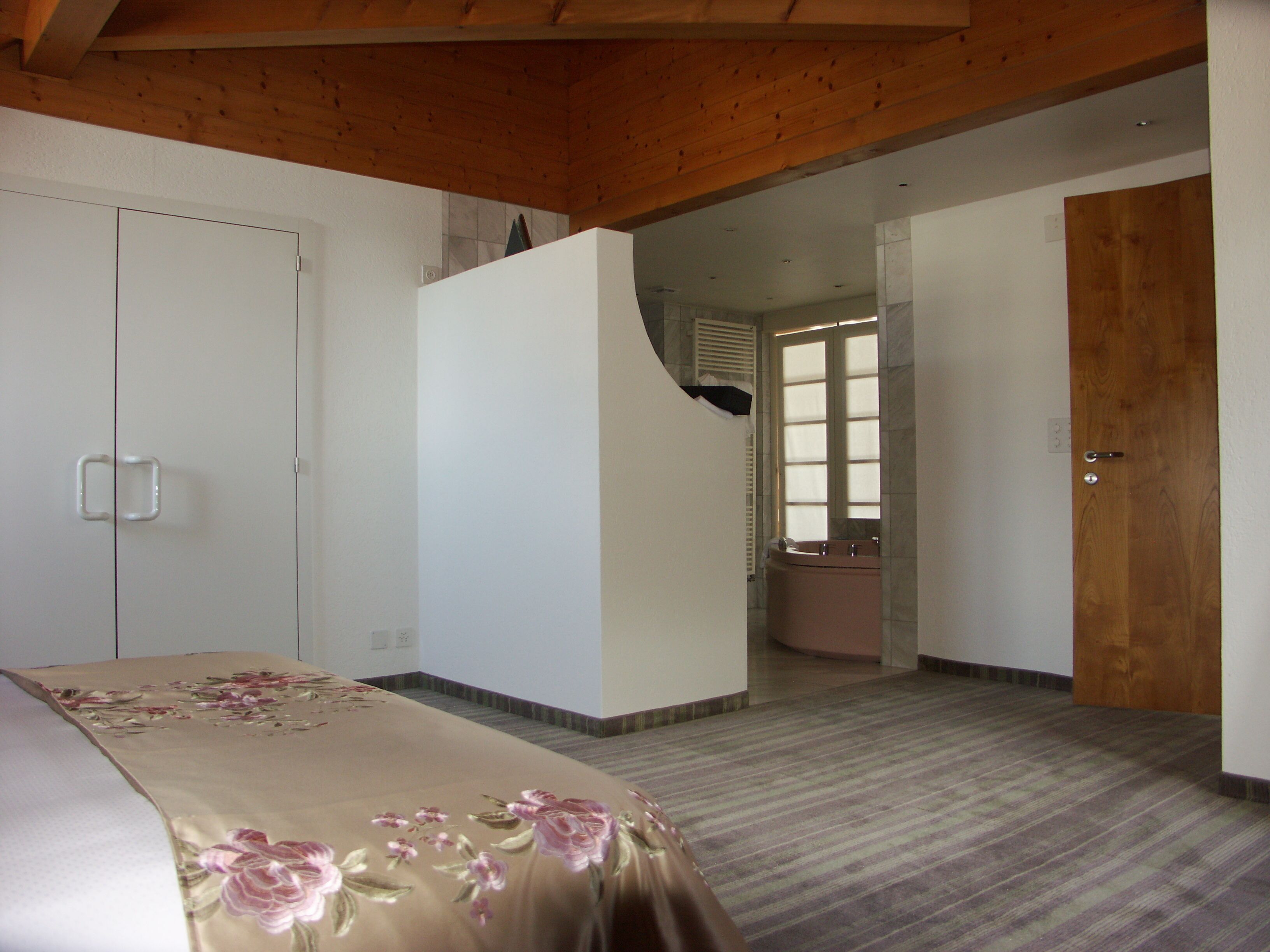 A bedroom with a bed, a wardrobe, and a bathroom visible through an open door.