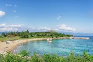 A beach with clear blue water, a sandy shore, and a stone pier extending into the sea. - Studio near the city centre (Vrbnik)