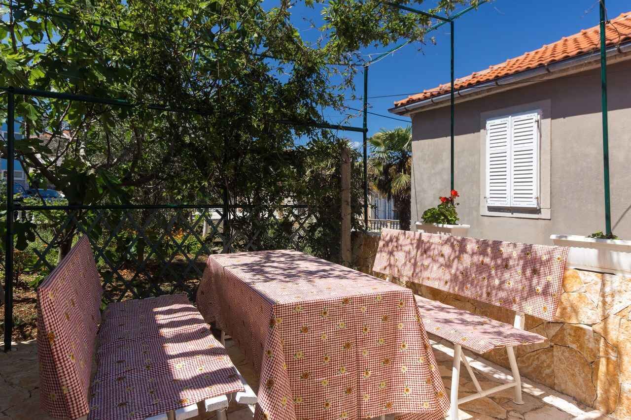 Un patio al aire libre con una mesa y bancos cubiertos con manteles a cuadros, rodeado por una valla de metal y árboles.