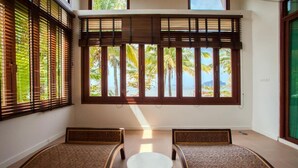 A room with a view of palm trees and the sea, featuring a round table and two cushioned seating areas. - Amatapura Beach 6 (Sai Thai)