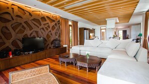 A modern living room with a wooden ceiling, a white sofa, a TV on a wooden stand, and a patterned rug. - Amatapura Beach 6 (Sai Thai)