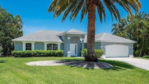 A single-story house with a garage, surrounded by a well-maintained lawn and palm trees.