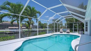 A swimming pool with a glass enclosure, surrounded by palm trees and a view of a residential area.