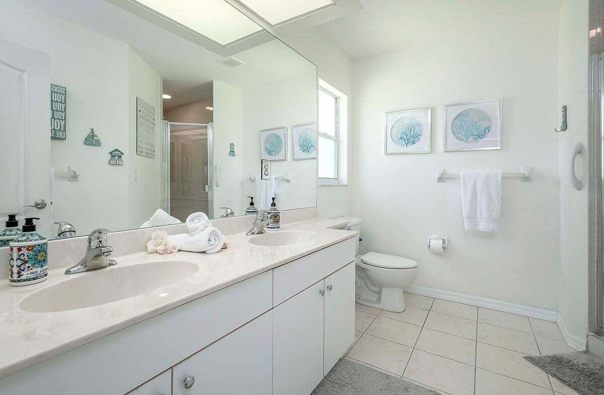 A modern bathroom with two sinks, a toilet, and a shower. There are framed pictures on the wall and a large mirror above the sink.