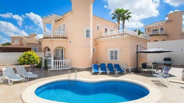 A building with a pool, blue lounge chairs, and a palm tree. - CH Villa Cuenca Atalaya Park (Benijofar) (Ciudad Quesada)