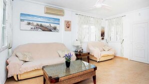 A living room with a beige sofa, a smaller armchair, a glass coffee table, and a painting on the wall. - CH Villa Cuenca Atalaya Park (Benijofar) (Ciudad Quesada)