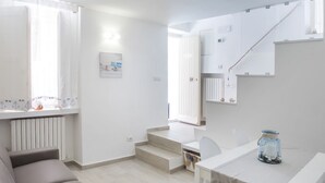 A modern, minimalist living space with a sofa, a dining table, and a staircase leading to an upper level. - S186 - Sirolo, wonderful sky-earth in the historic center (Sirolo)