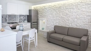 A modern kitchen with white cabinets, a dining area with a white table and chairs, and a beige sofa against a textured wall. - S186 - Sirolo, wonderful sky-earth in the historic center (Sirolo)
