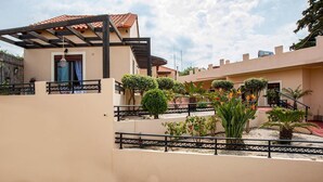 A two-story building with a covered patio area, a staircase, and a garden with various plants and a bird of paradise flower. - Kyriaki' s Cozy Appartment (Chania)