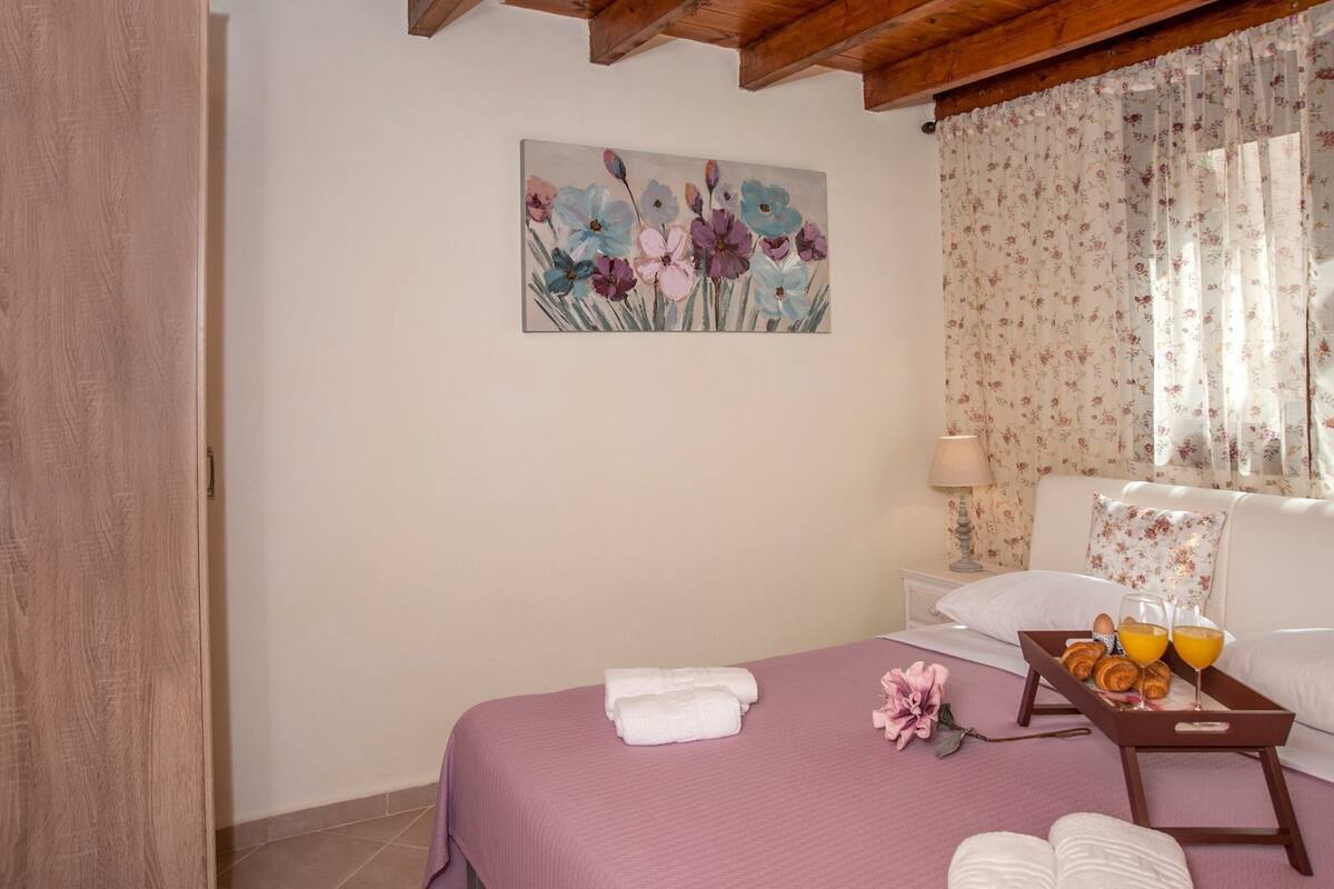 A bedroom with a bed, a painting, a tray with breakfast items, and a window with curtains.