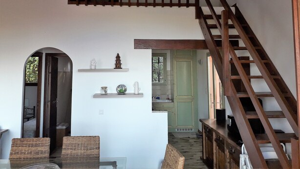 A spacious living area with a wooden staircase, a dining table with chairs, and a kitchen visible through an open doorway. - T4 plus T2 independent. (Pietrosella)
