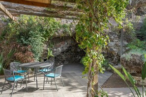 A patio with a stone wall, a table with chairs, and a hanging vine. - Secluded Casita in Sunny Southeast with Private Pool, Terrace and Barb (Candelaria)