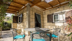 Une terrasse couverte avec une table ronde et quatre chaises, des murs en pierre et un plafond en bois.