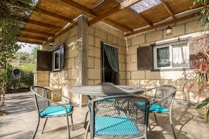 Un patio cubierto con una mesa redonda y cuatro sillas, paredes de piedra y techo de madera.