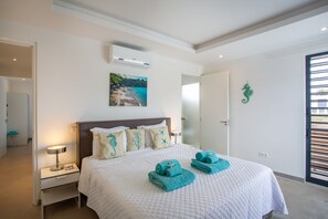A neatly made bed with a white quilt, two rolled towels, and a seahorse decoration on the wall.
