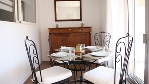 A dining area with a round table, four chairs, and a wooden cabinet with a mirror above it. - Le Renoir (Nice)