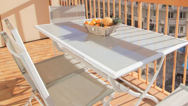 A balcony with a white table and chairs, a fruit basket, and a view of a multi-story building. - Le Renoir (Nice)