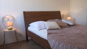 A neatly made bed with a wooden headboard, two bedside lamps, and a small table with a lamp. - Le Renoir (Nice)