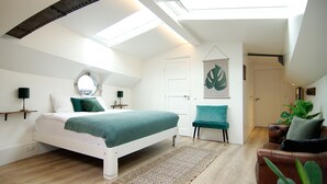 Una camera da letto con un lucernario, un letto con biancheria verde, una sedia, un divano e una pianta grande.