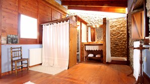 A wooden cabin interior with a wooden chair, a white curtain, a stone wall, and a wooden table.