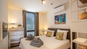 Camera d'albergo con un letto, comodini, una lampada, una finestra con tende, un condizionatore d'aria a parete e un quadro.