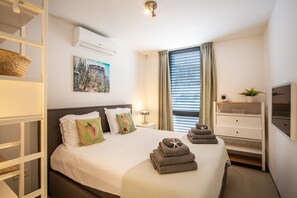 Une chambre d’hôtel bien rangée, avec un lit, une table de chevet, une lampe, un téléviseur et une fenêtre avec des rideaux.