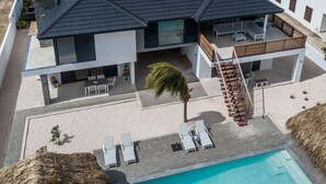 Una moderna casa a due piani con piscina, area salotto esterna e una scala che conduce a un patio.