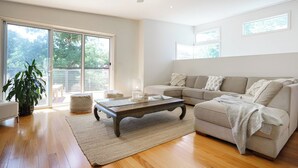 Ein geräumiges Wohnzimmer mit einem großen Schiebeglasfenster, das auf einen Balkon führt, ein beiges Sofa, ein Holztisch und ein Blumentopf.