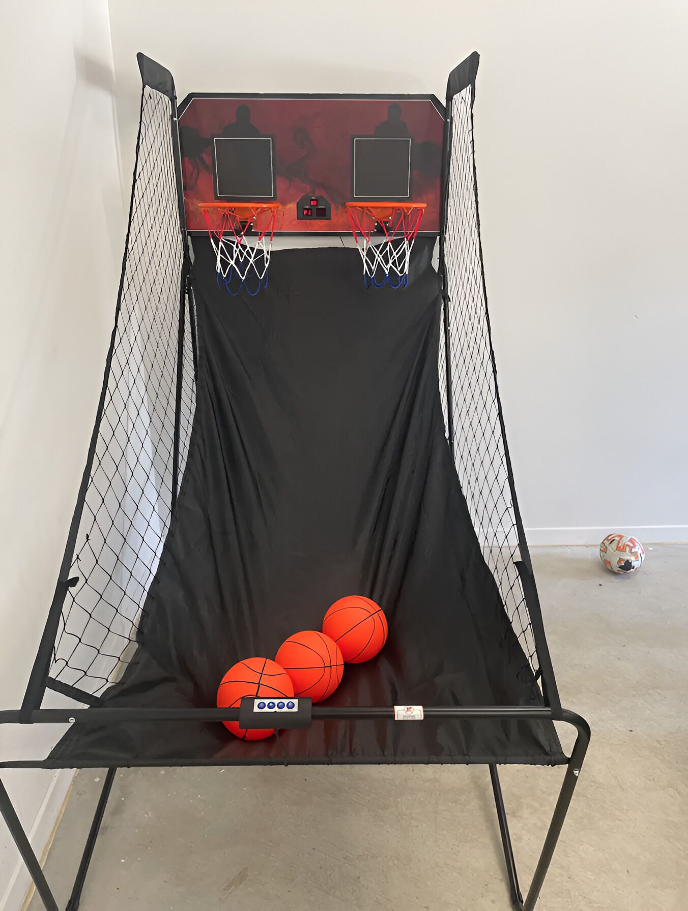 A basketball shooting net with three basketballs and a soccer ball on the ground.