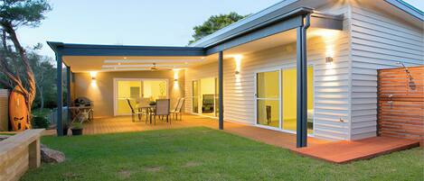 A modern house with a covered patio, a dining area, and a large sliding glass door leading to a living room.