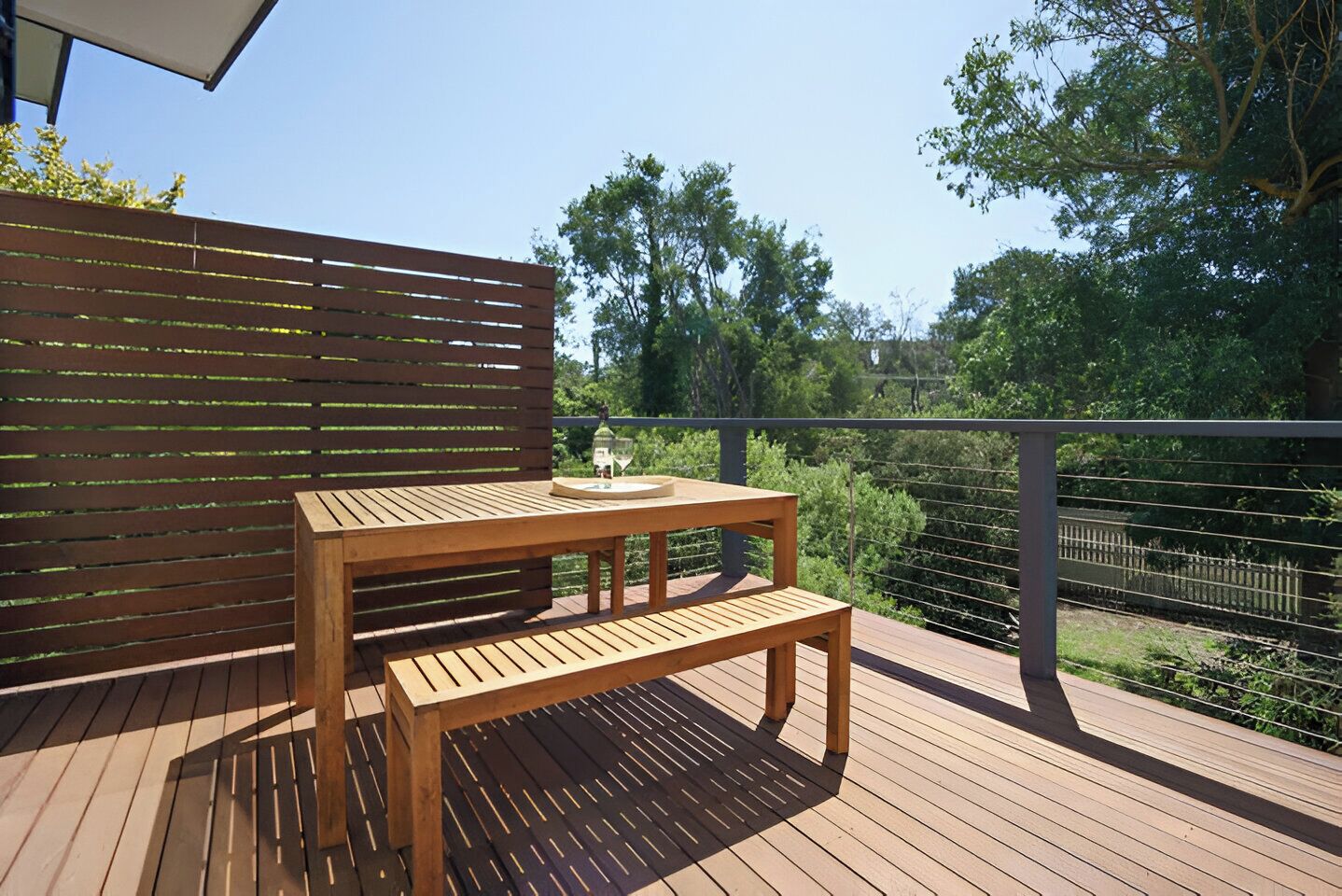 A wooden deck with a table and bench, surrounded by a fence and trees.