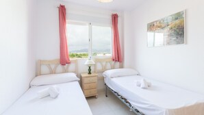 A twin room with two beds, a bedside table with a lamp, and a window with curtains. - BEGONIA - Apartment with sea views in Daimuz. Free WiFi (Daimús)