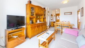 A living room with a television, wooden cabinet, dining table, and chairs. - BEGONIA - Apartment with sea views in Daimuz. Free WiFi (Daimús)